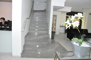 A staircase leading to a second floor, a reception area with a counter, and a potted orchid plant. - Hotel Nacional (Rondonopolis)