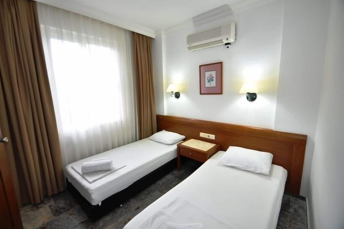 Una habitación de hotel con dos camas individuales, un cabecero de madera, una mesita de noche, un aire acondicionado de pared y dos lámparas de pared.