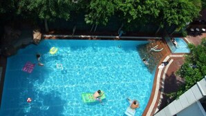 Una piscina con agua cristalina, rodeada de árboles y un edificio blanco.
