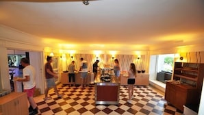 Una cocina de hotel con piso a cuadros, una isla central y un grupo de personas alrededor de una mesa de buffet.
