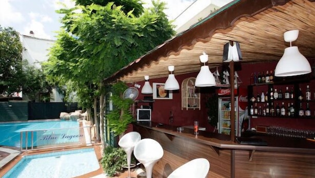 Zona de bar junto a la piscina con techo de madera, lámparas colgantes blancas y una barra repleta de botellas.