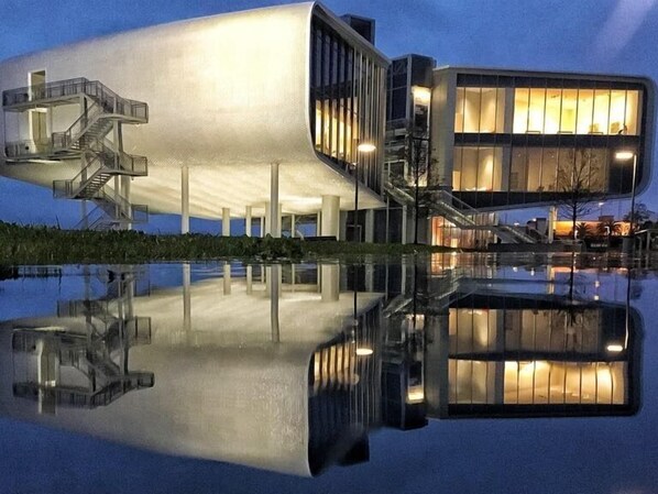 Ein modernes Gebäude mit einem einzigartigen, geschwungenen Design, einer Glasstiege und einem Spiegelbild im Wasser.