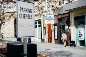 Una escena callejera con un letrero que dice 'PARKING CLIENTES' y un edificio con escaparate.