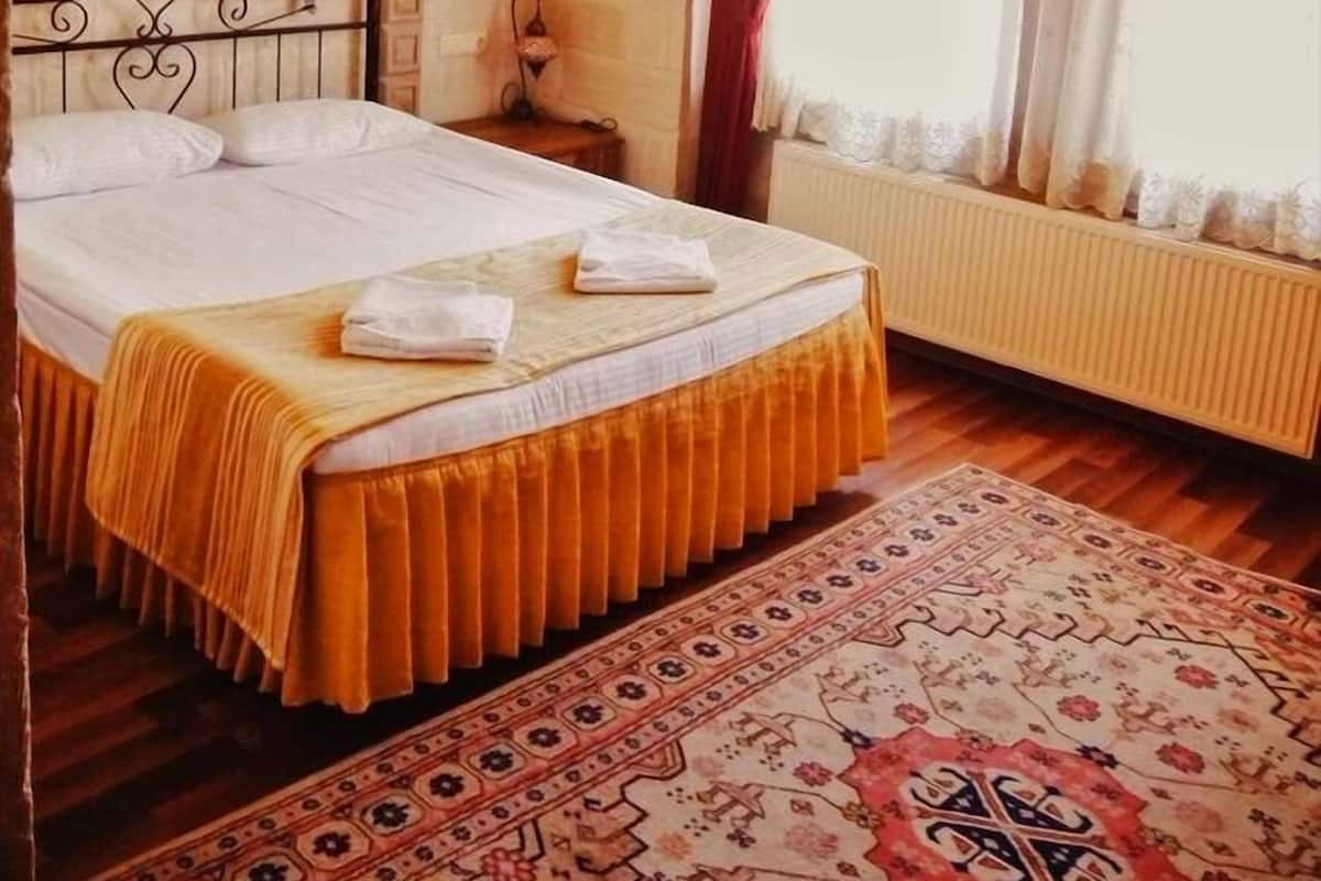 Ein traditionell eingerichteter Raum mit einem Bett, einem Heizkörper, einem Fenster mit Vorhängen und einem gemusterten Teppich.