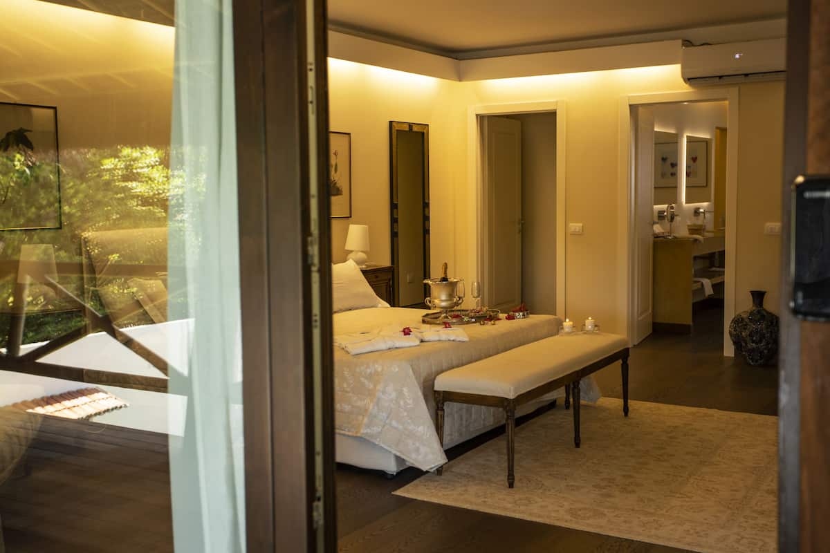 Une chambre à coucher comprenant un lit, une table de chevet, un banc et donnant sur l’extérieur.