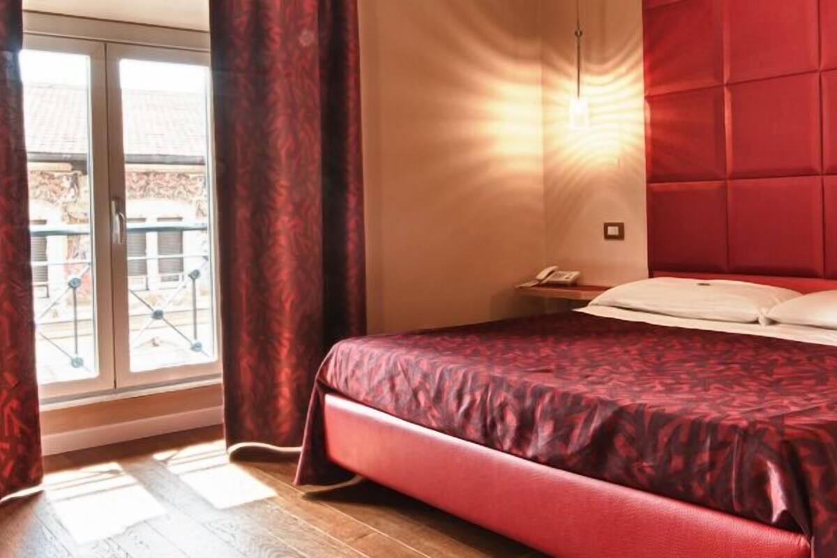 A bedroom with a bed, curtains, a window, and a wall-mounted light.