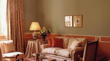 Una sala de estar acogedora con sofá, sillón y mesa de centro, que incluye una araña, cortinas y cuadros en la pared.