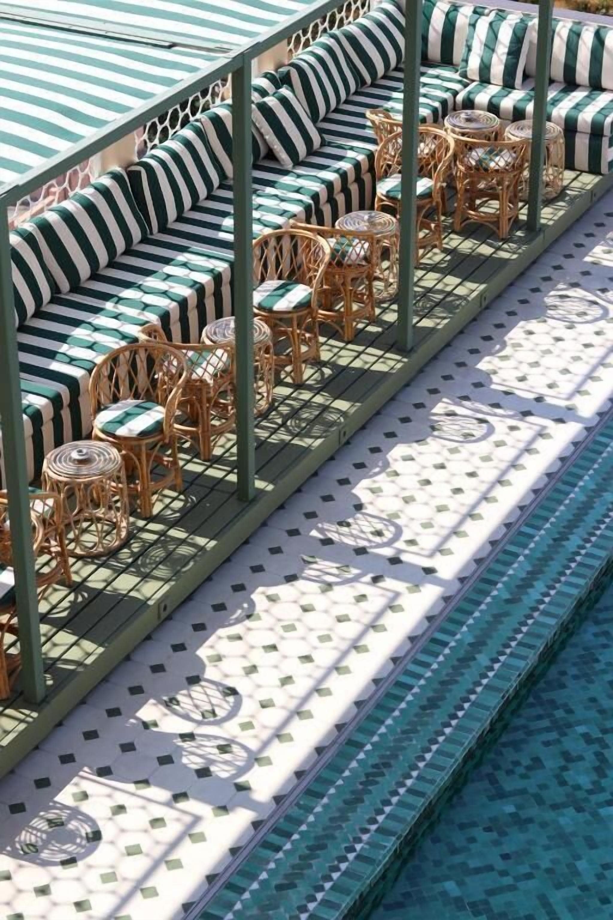 Un área junto a la piscina con cojines a rayas y sillas de mimbre.