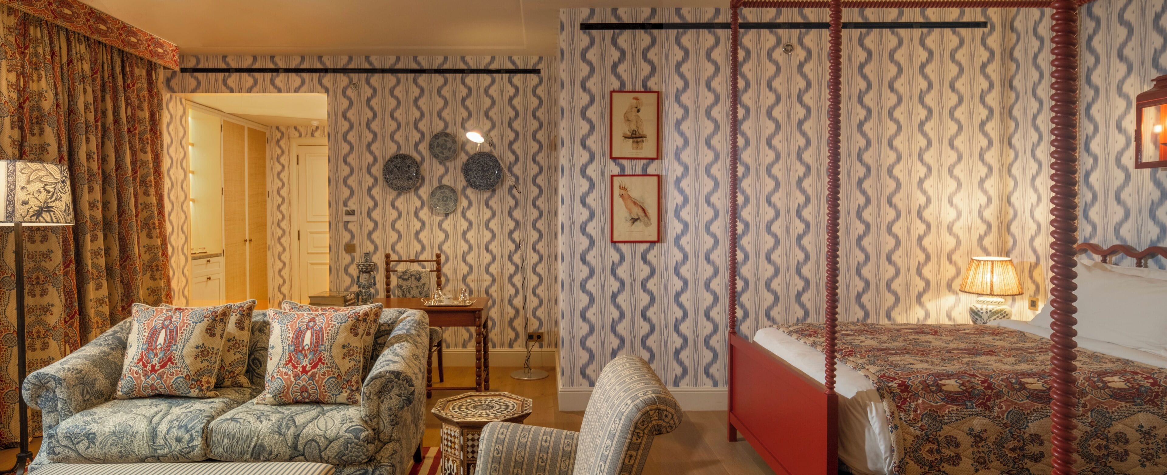 Una habitación con papel tapiz estampado, una cama con dosel, un sofá con cojines estampados y una mesita auxiliar.