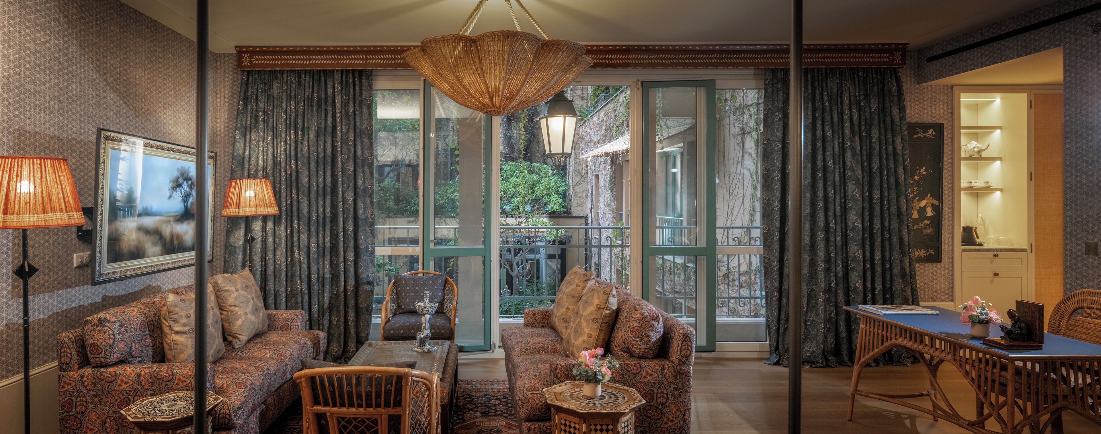 A cozy living room with patterned sofas, a dining table, and a view of a garden through large sliding doors.