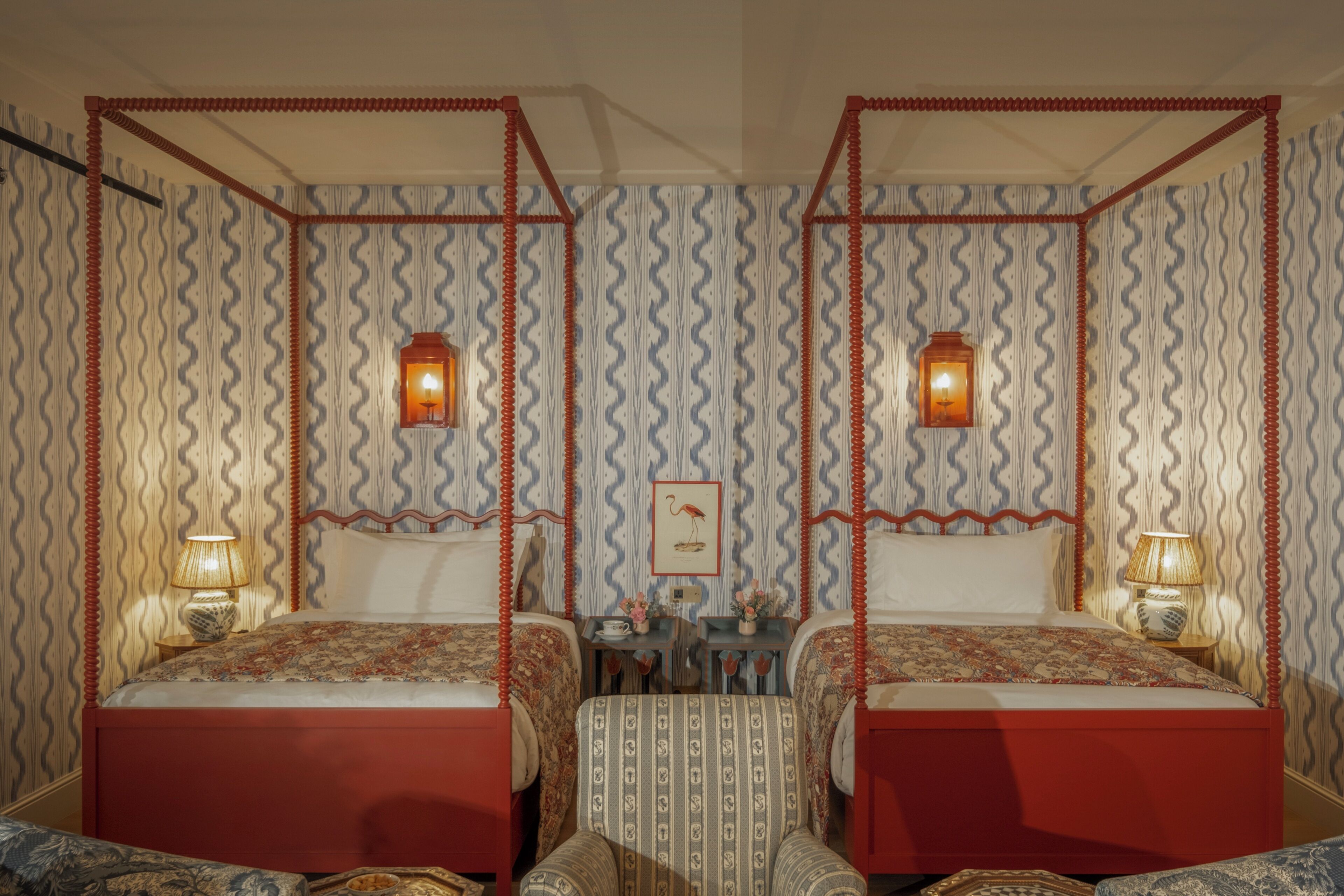 A room with two beds, each with a canopy, and a small table with a lamp.