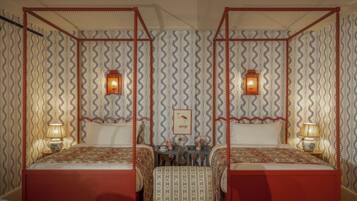 A room with two beds, each with a canopy, and a small table with a lamp.