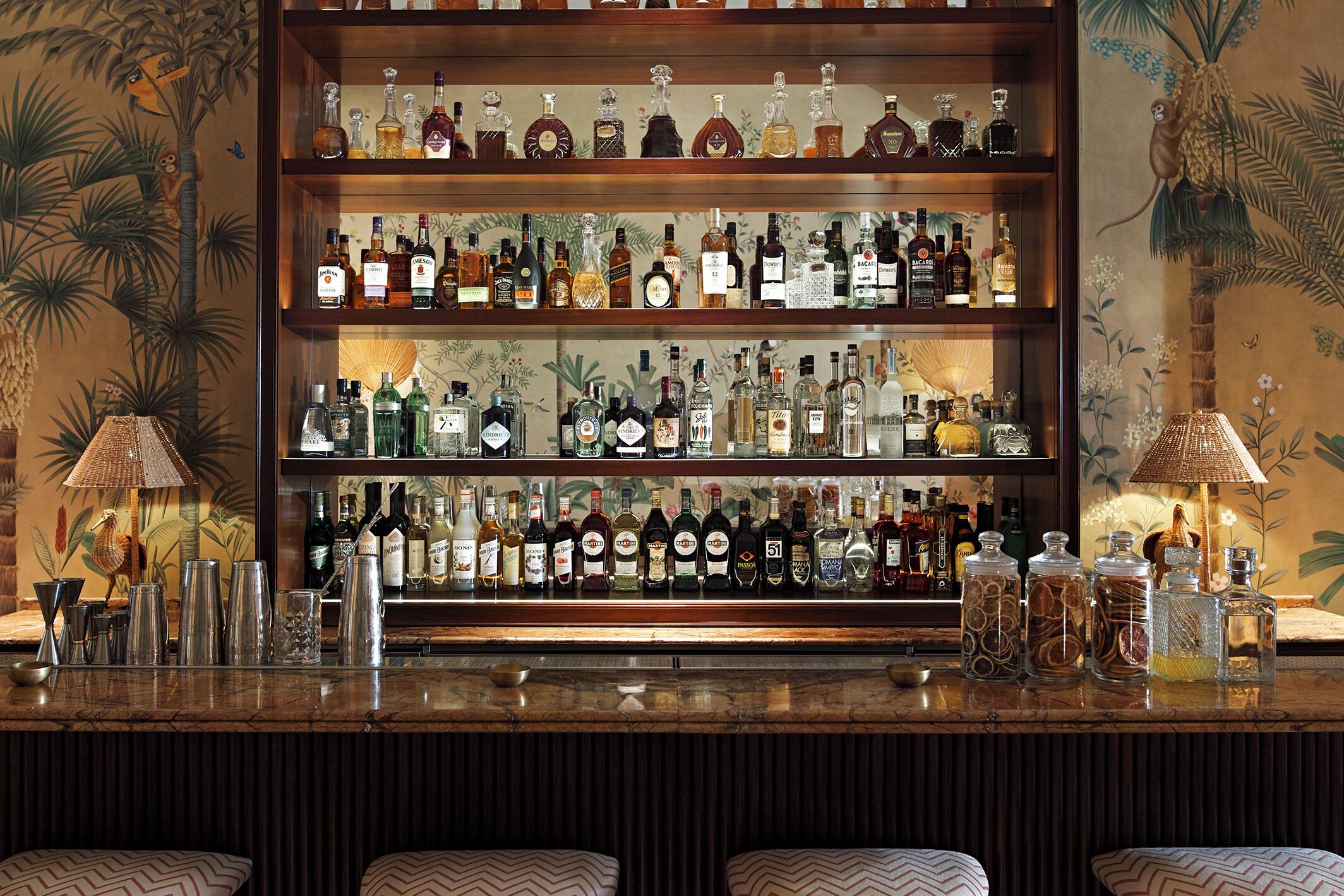 A bar with multiple shelves of liquor bottles, a bar counter, and two lamps.