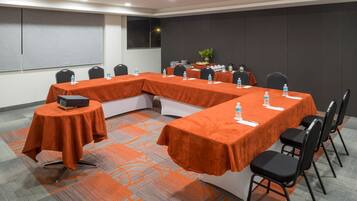 A conference room with a long table covered in orange cloth, surrounded by black chairs, and equipped with water bottles and a laptop.