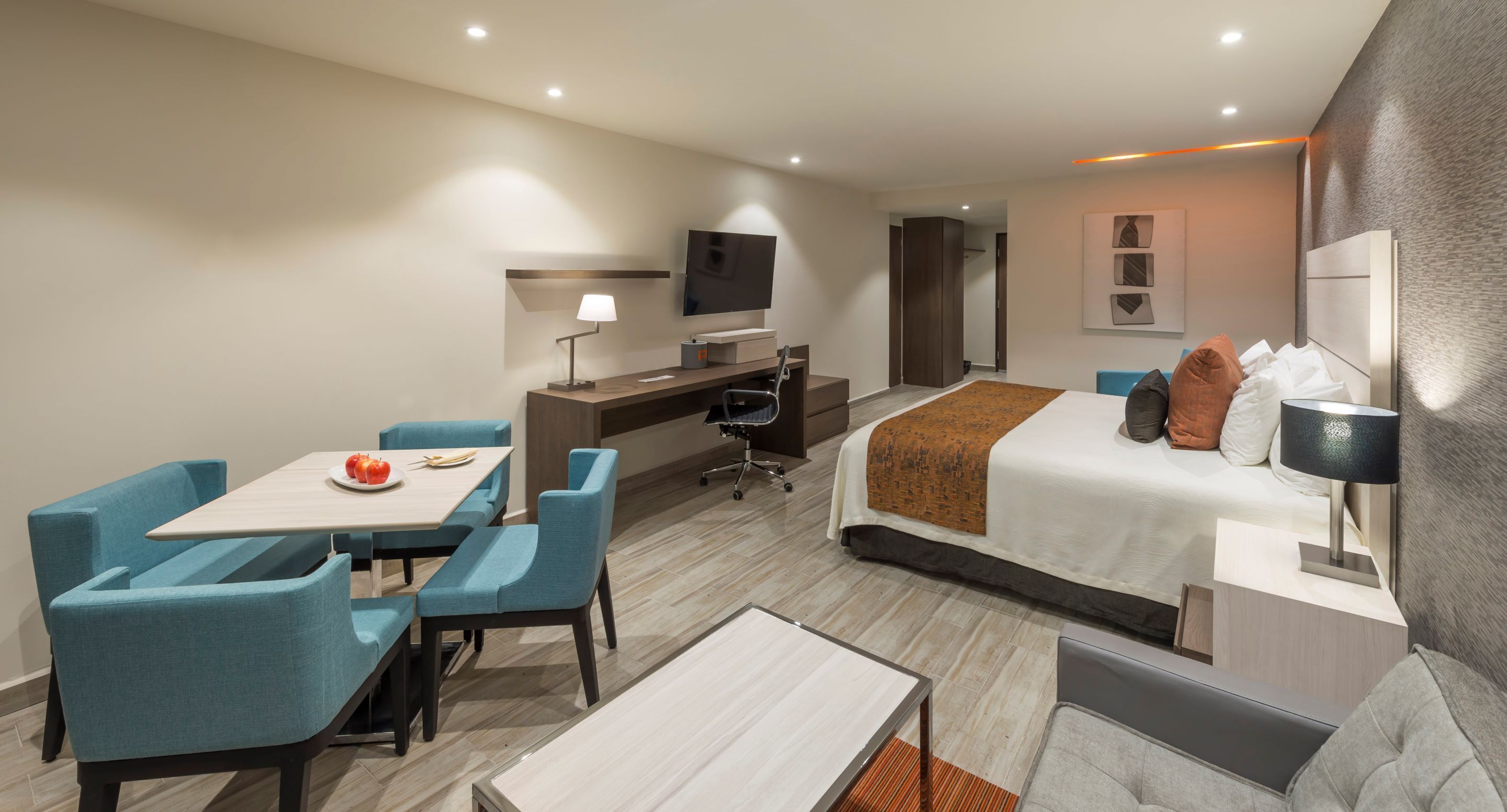 A hotel room with a bed, a desk, a TV, a dining table with chairs, and a sofa.