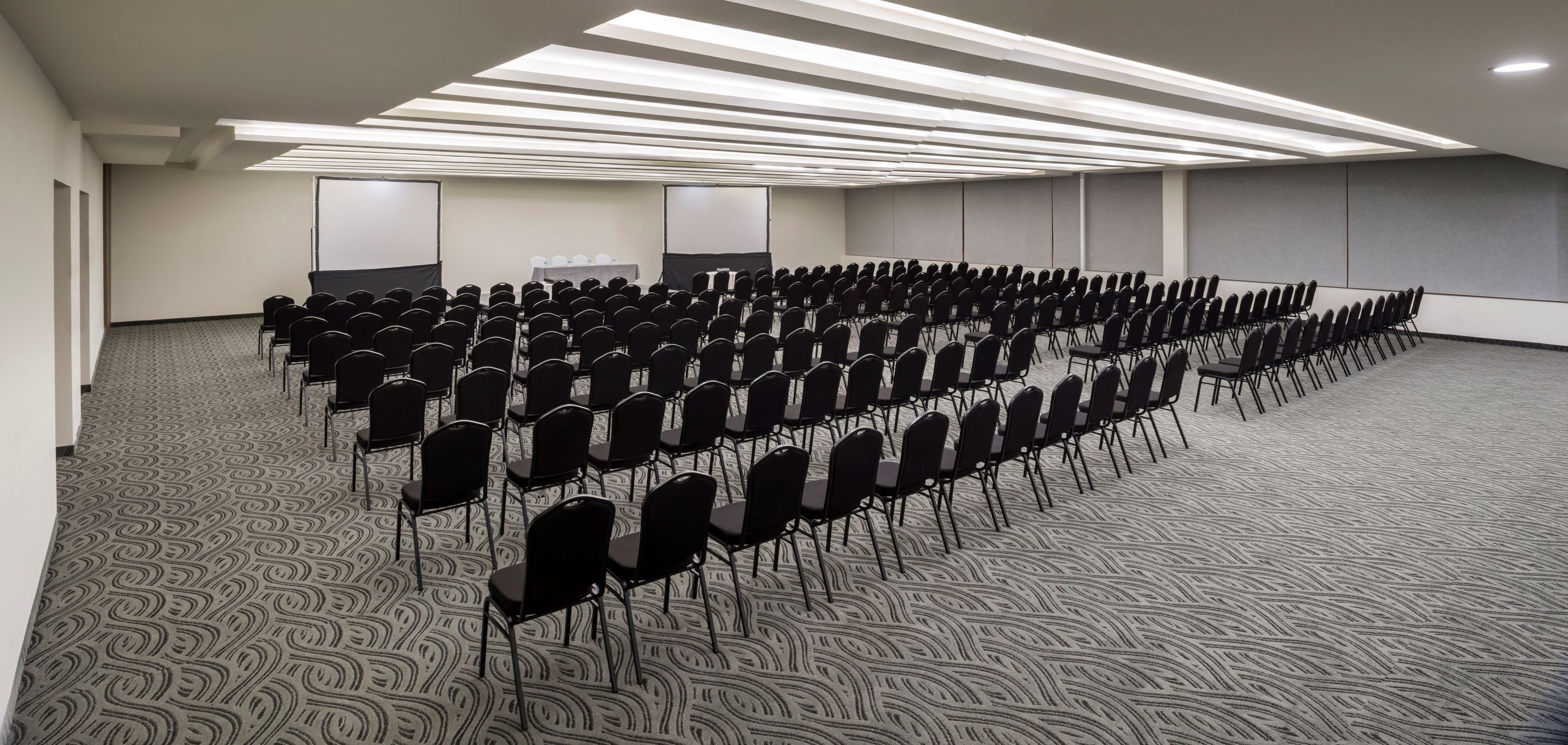 A conference room with rows of chairs, a projector screen, and a carpeted floor.