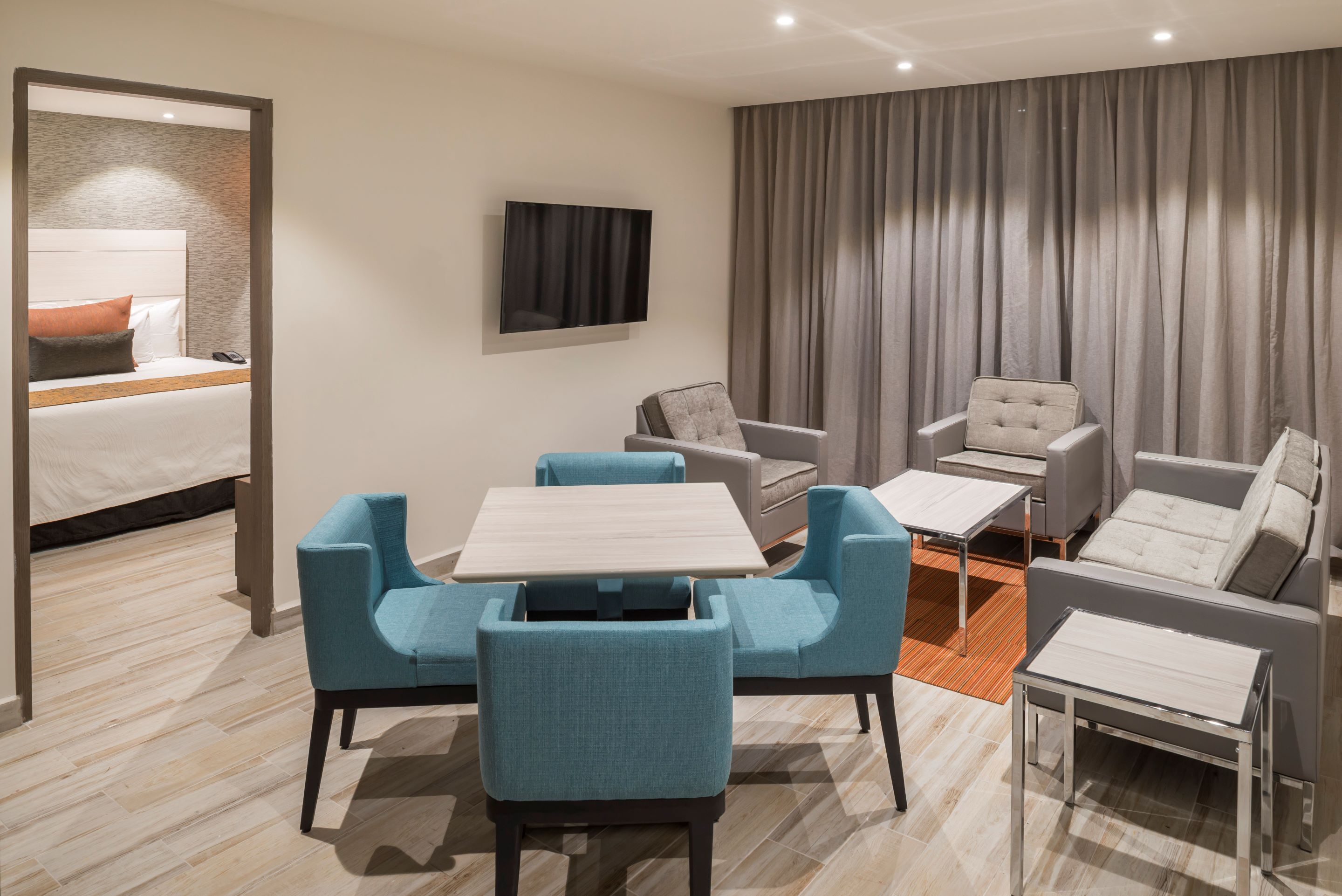 Une chambre d’hôtel moderne équipée d’un lit, d’une télévision, d’un coin repas avec des chaises et d’un canapé.
