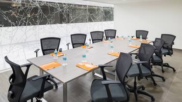 Uma sala de conferências com uma mesa comprida, cadeiras pretas e garrafas de água sobre a mesa.