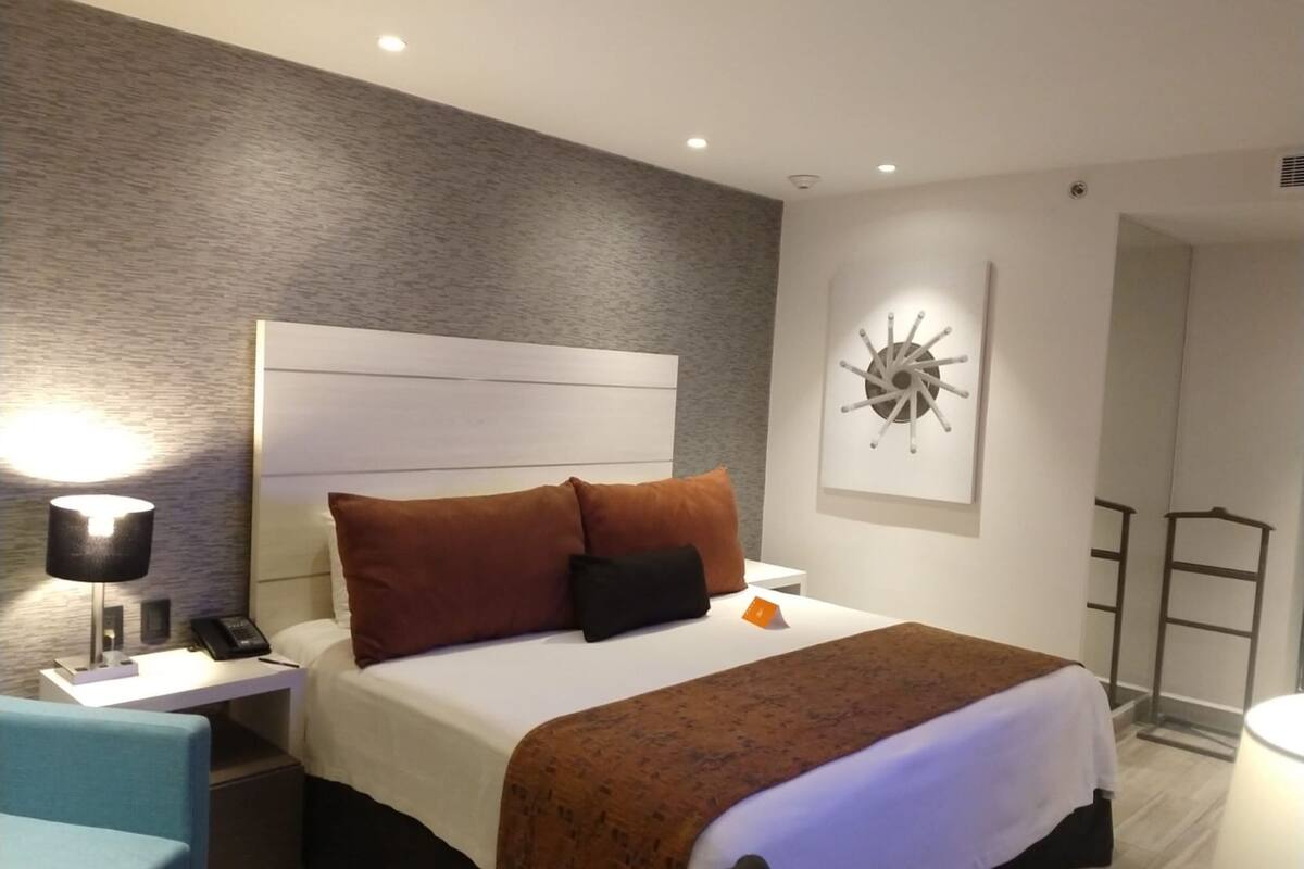 Une chambre d’hôtel moderne équipée d’un lit, d’une table de chevet, d’une lampe et d’une œuvre d’art accrochée au mur.