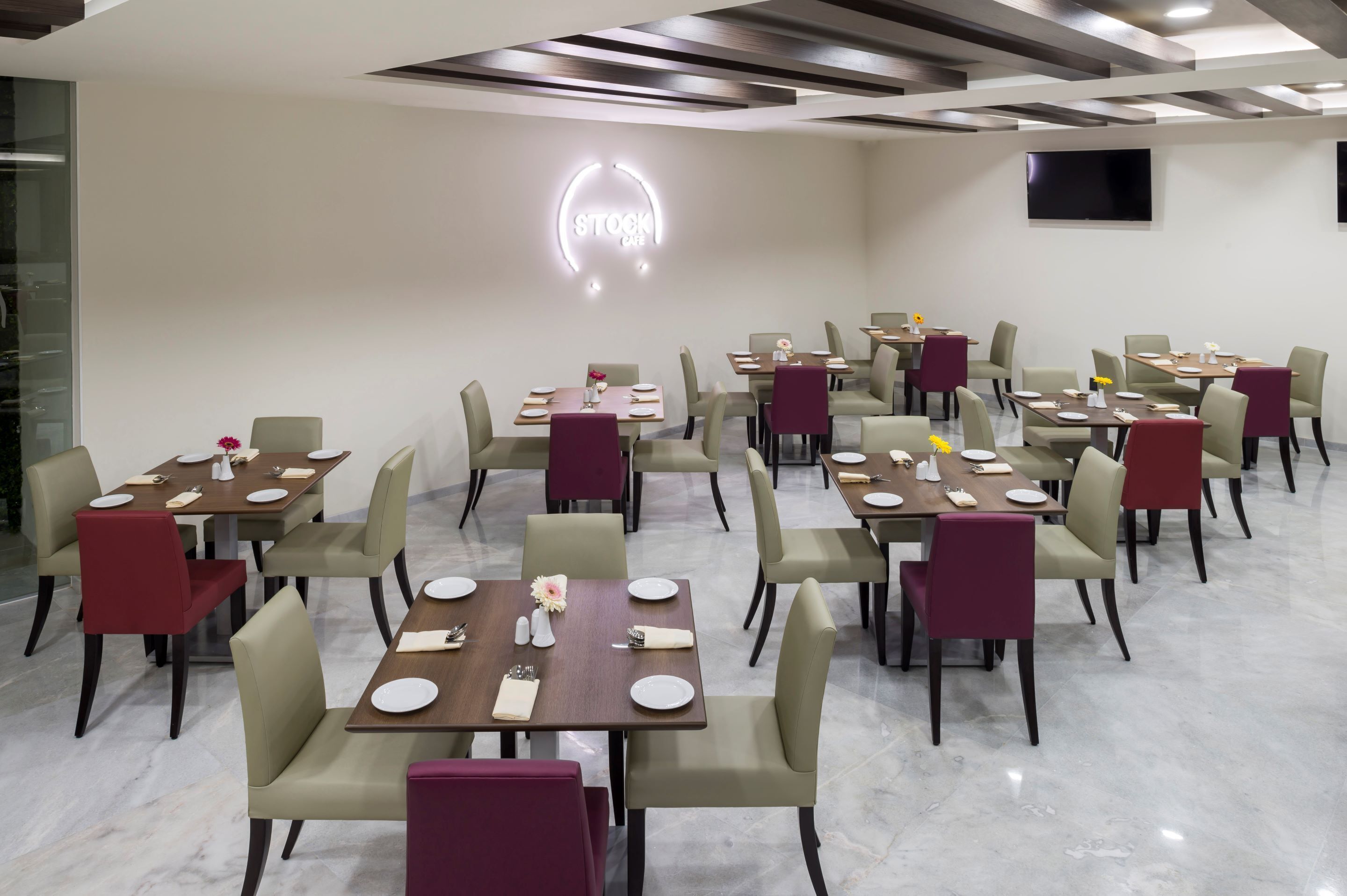 A dining area with multiple tables and chairs, a neon sign on the wall, and a flat-screen TV mounted on the wall.
