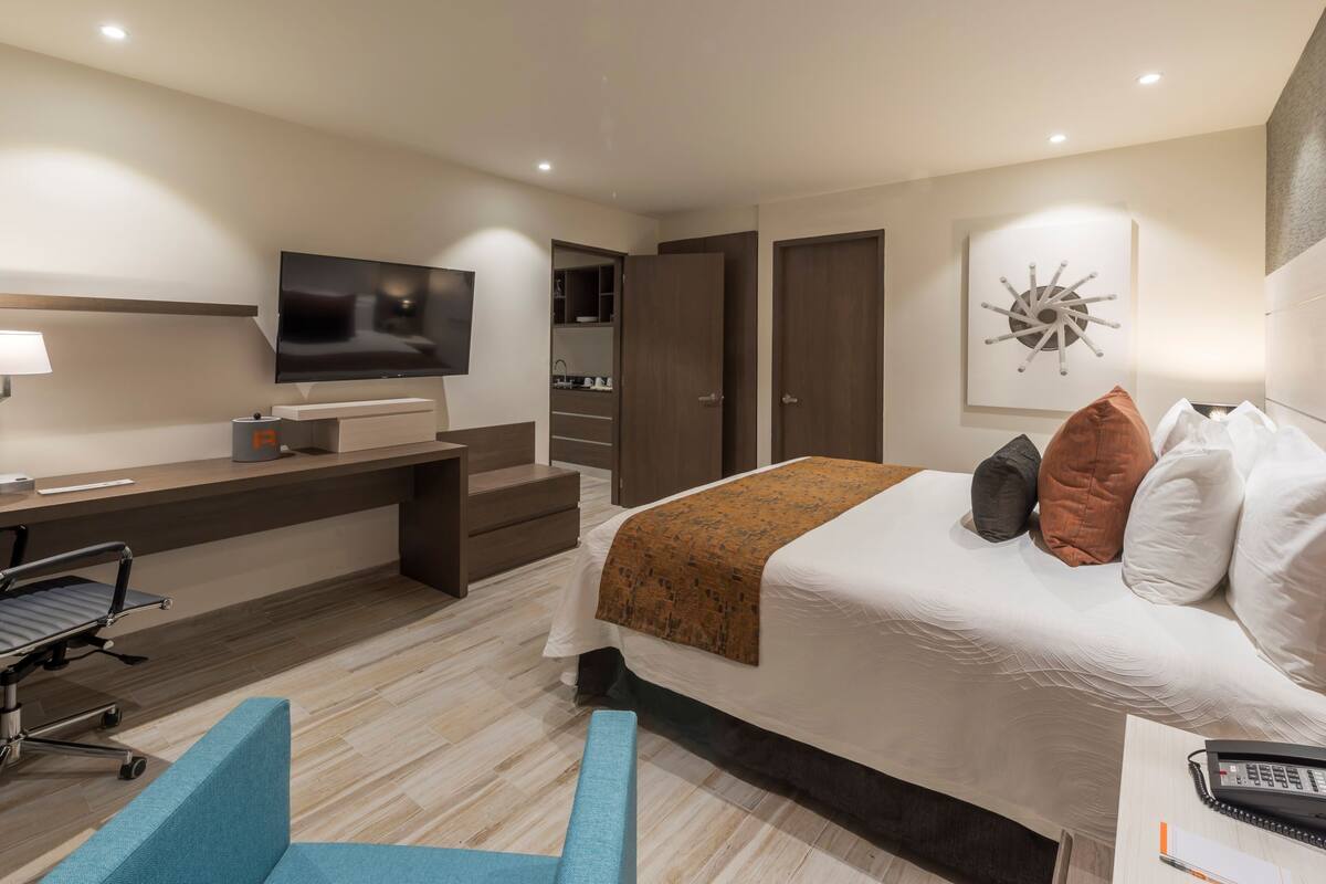 Une chambre d’hôtel moderne équipée d’un lit, d’un bureau, d’une chaise, d’une télévision et d’une salle de bain.