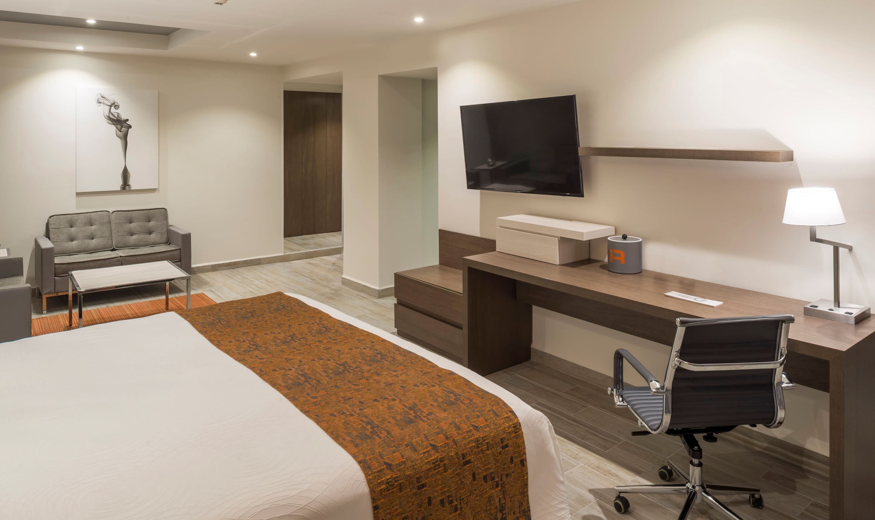 Een moderne hotelkamer met een bed, een bureau, een stoel, een televisie en een lamp.