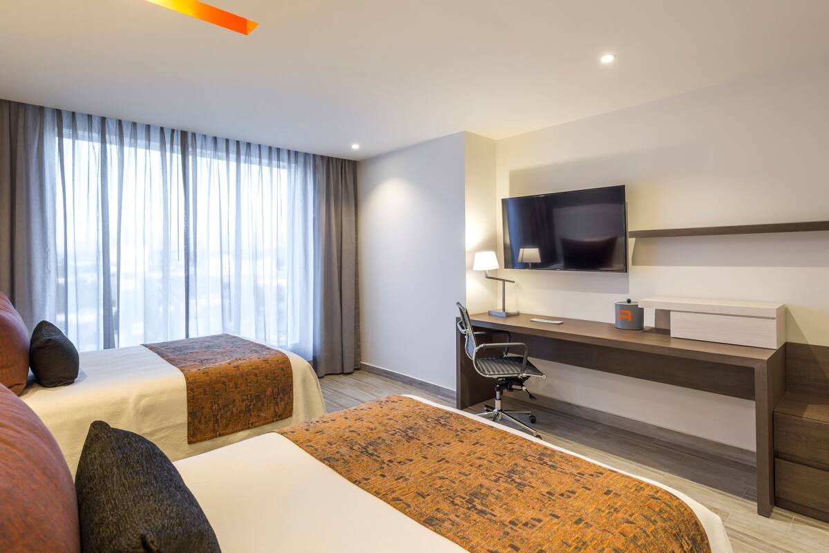Une chambre d’hôtel avec deux lits, un bureau, une chaise, une télévision et une fenêtre avec des rideaux.
