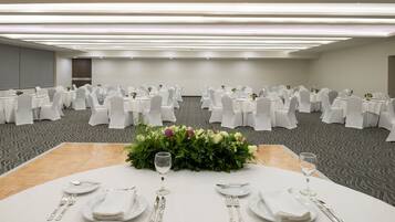 A banquet hall with round tables set for dining, white tablecloths, and chairs with white covers.
