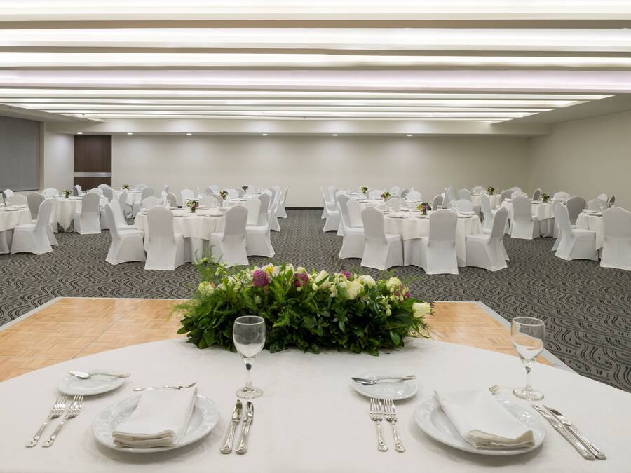 A banquet hall with round tables set for dining, white tablecloths, and chairs with white covers.