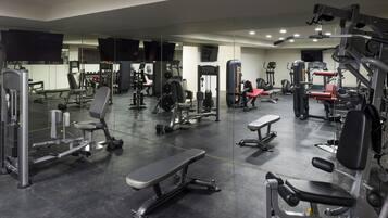 Ett gym med olika typer av träningsredskap, en bänk och en vägg med speglar.