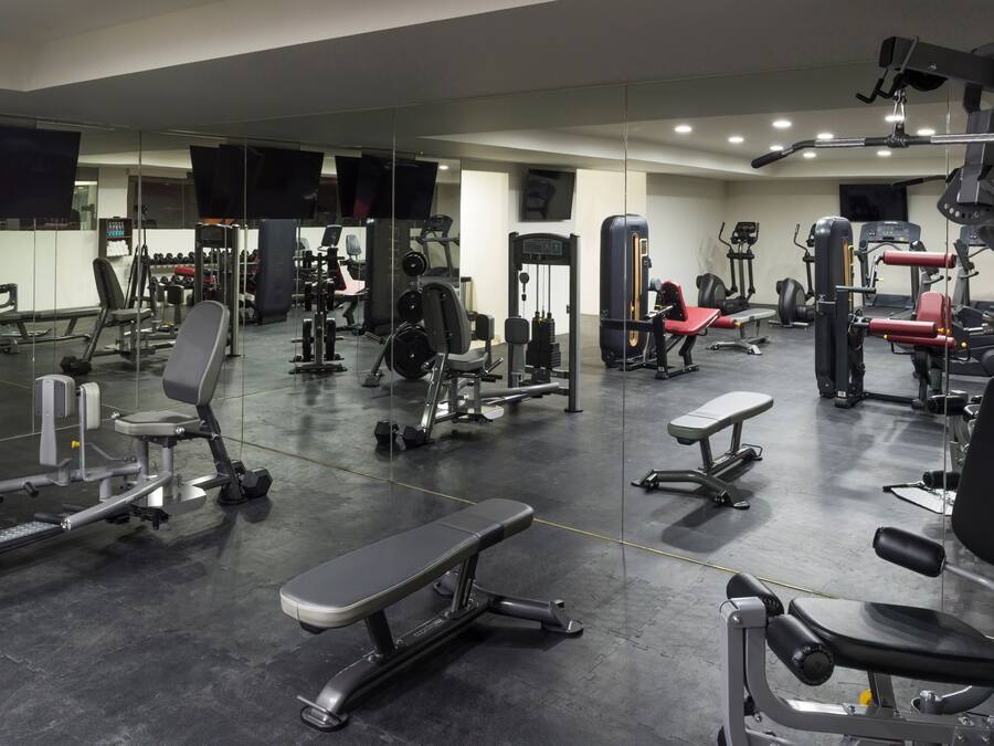 Ett gym med olika typer av träningsredskap, en bänk och en vägg med speglar.