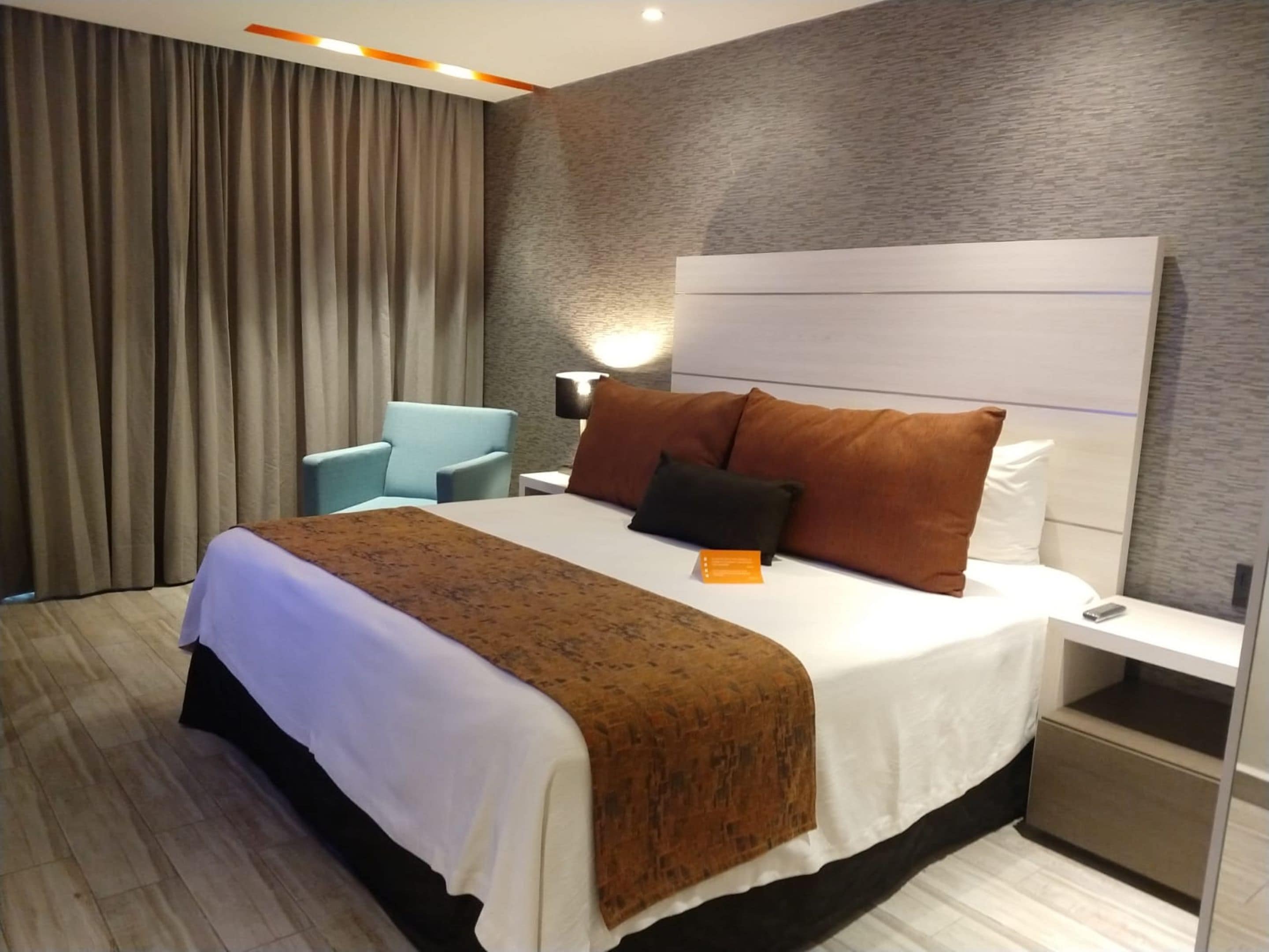 Una habitación de hotel con cama, mesita de noche, lámpara, silla y cortina.