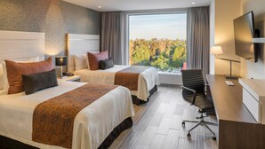 Une chambre d’hôtel avec deux lits, un bureau, une chaise, une télévision et une grande fenêtre donnant sur la ville.