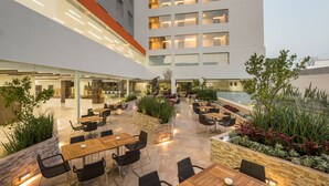 Un espace de restauration extérieur moderne, doté de plusieurs tables et chaises, entouré de jardinières et d’un mur en pierre.