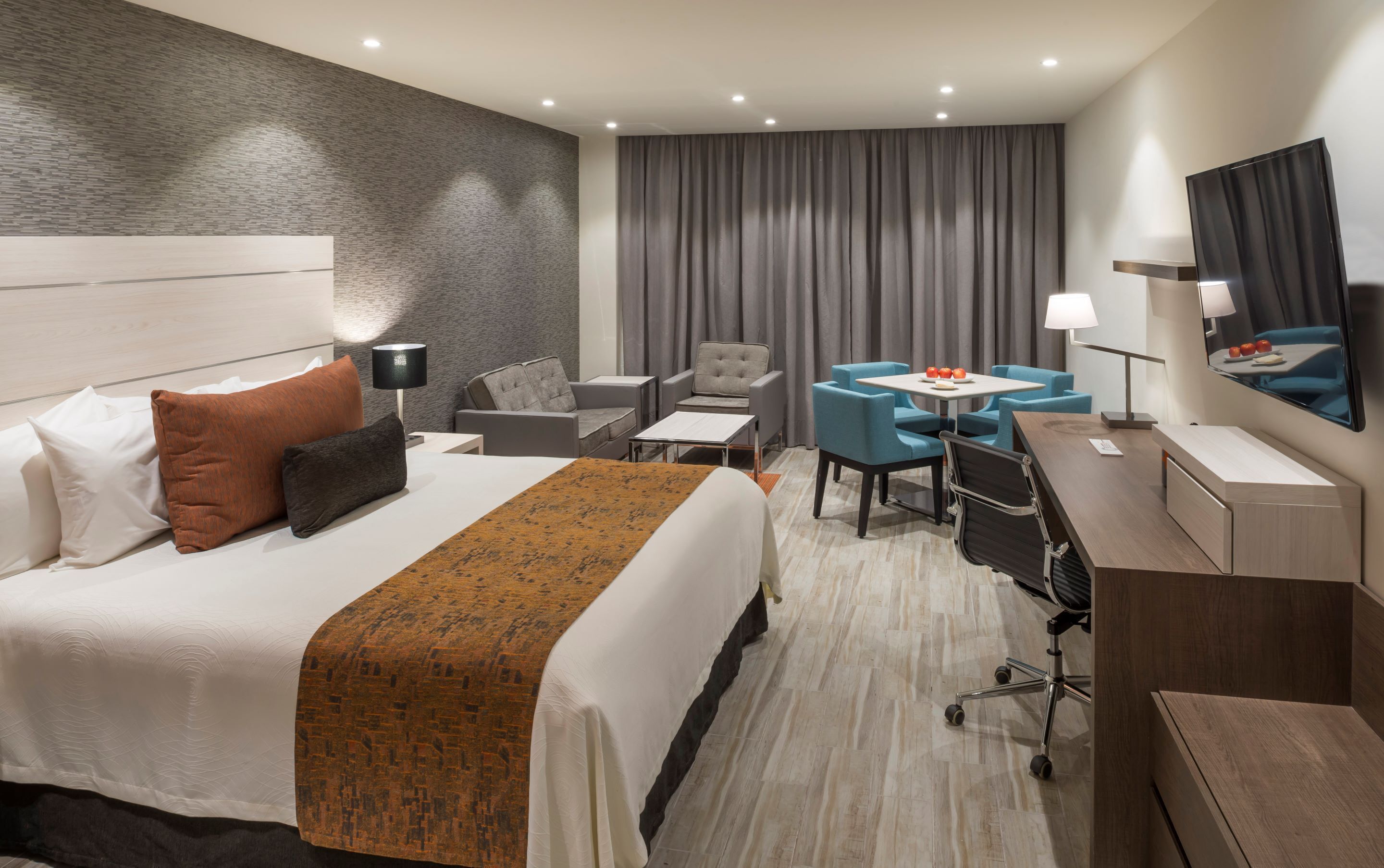 Une chambre d’hôtel avec un grand lit, un bureau, deux chaises, une petite table, une lampe, une télévision et un rideau.