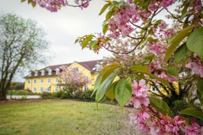 A yellow building with a symmetrical facade, surrounded by a well-maintained lawn and blooming pink trees. - Ferien Hotel Fläming (Rabenstein/Fläming)