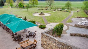 Eine Terrasse mit Sitzgelegenheiten im Freien, einem Brunnen und Blick auf ein grünes Feld.