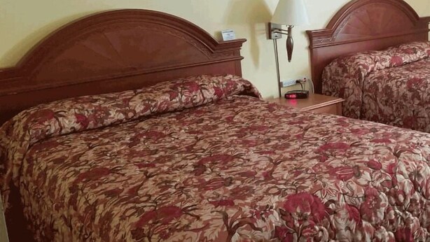 Une chambre d’hôtel avec deux lits, chacun agrémenté de draps à motifs floraux, une table de chevet avec une lampe et deux œuvres d’art encadrées accrochées au mur.