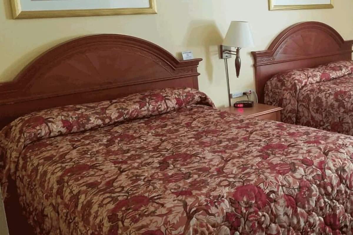 Una habitació d'hotel amb dos llits, cada un amb roba de llit de motius florals, una taula de nit amb una làmpada, i dos quadres penjats a la paret.