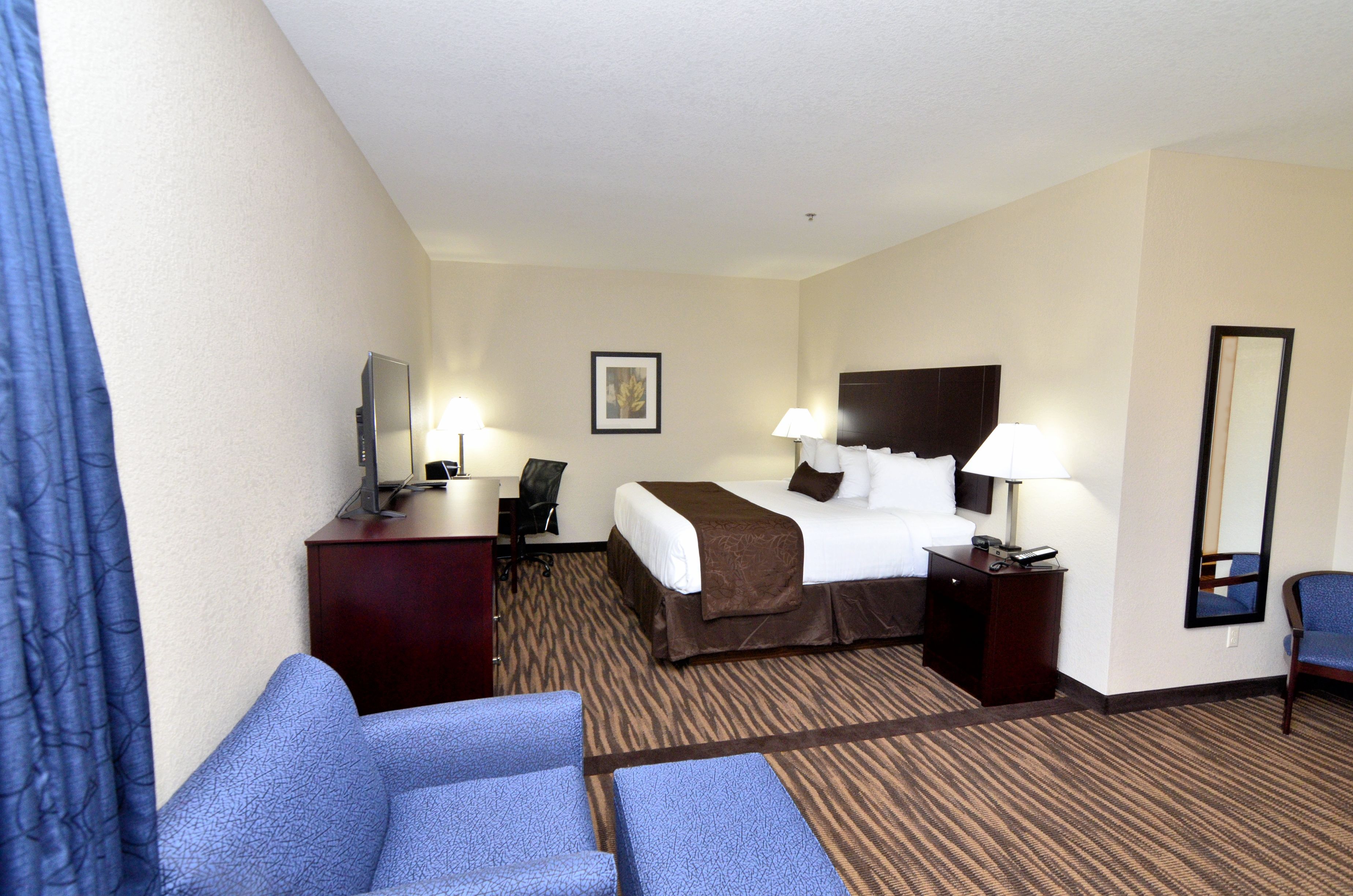 A hotel room with a bed, two bedside tables, a desk with a chair, a TV, and a large mirror.