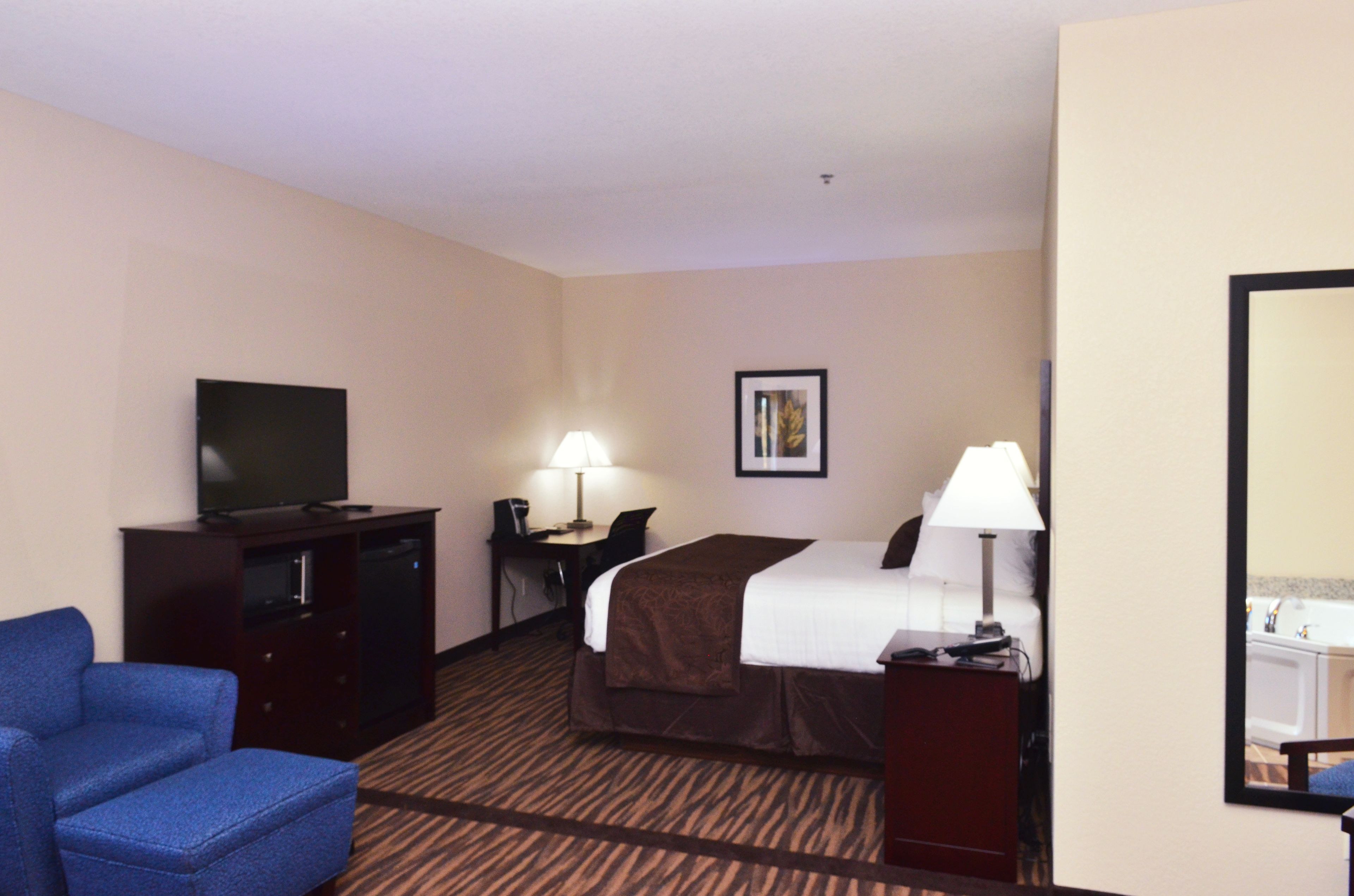 A hotel room with a bed, a desk with a lamp, a television, and a chair.