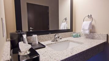 A hotel bathroom with a granite countertop, a sink, a mirror, and a towel rack.