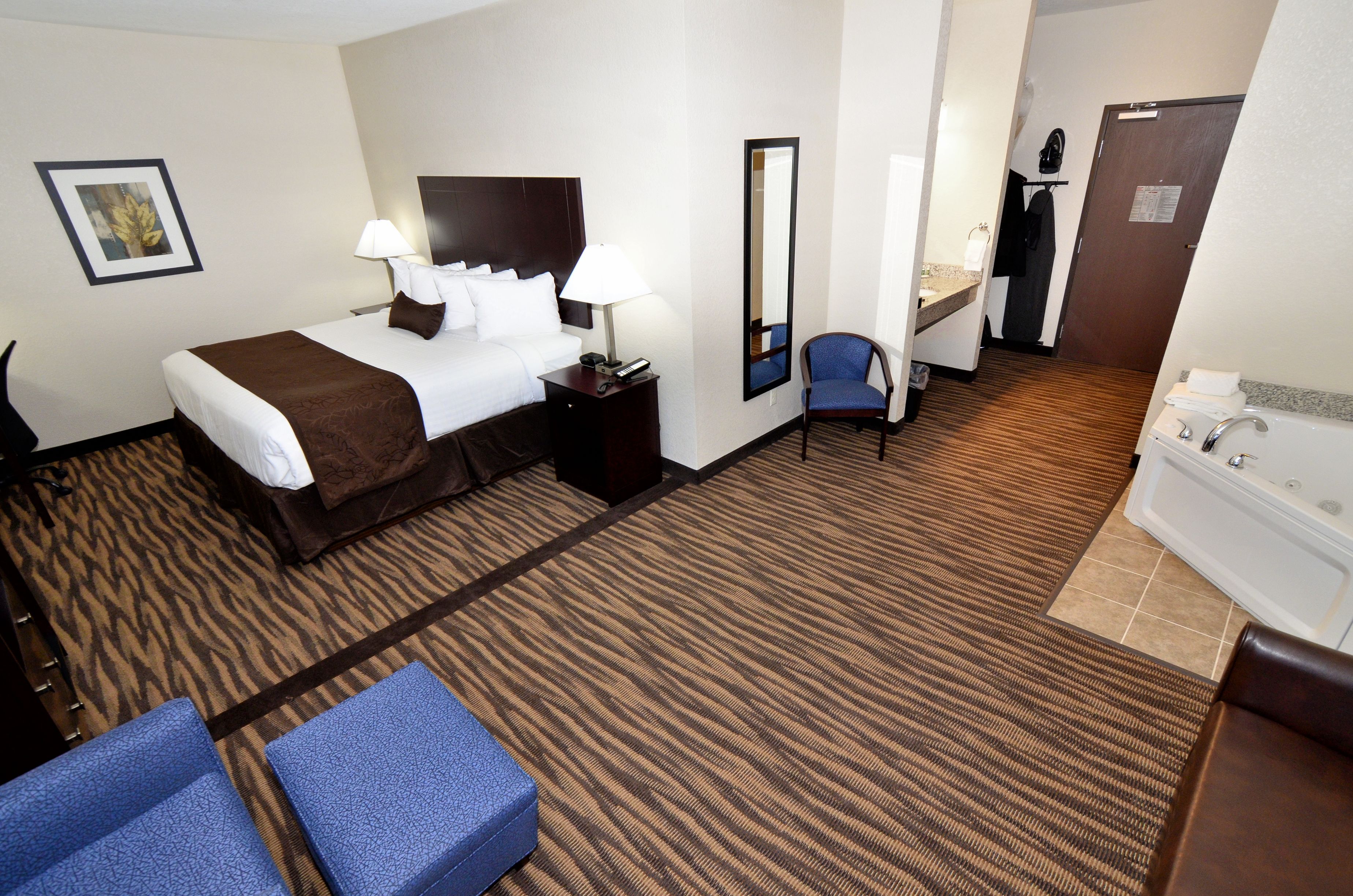 Habitación de hotel con cama, escritorio, silla y baño con bañera y espejo.