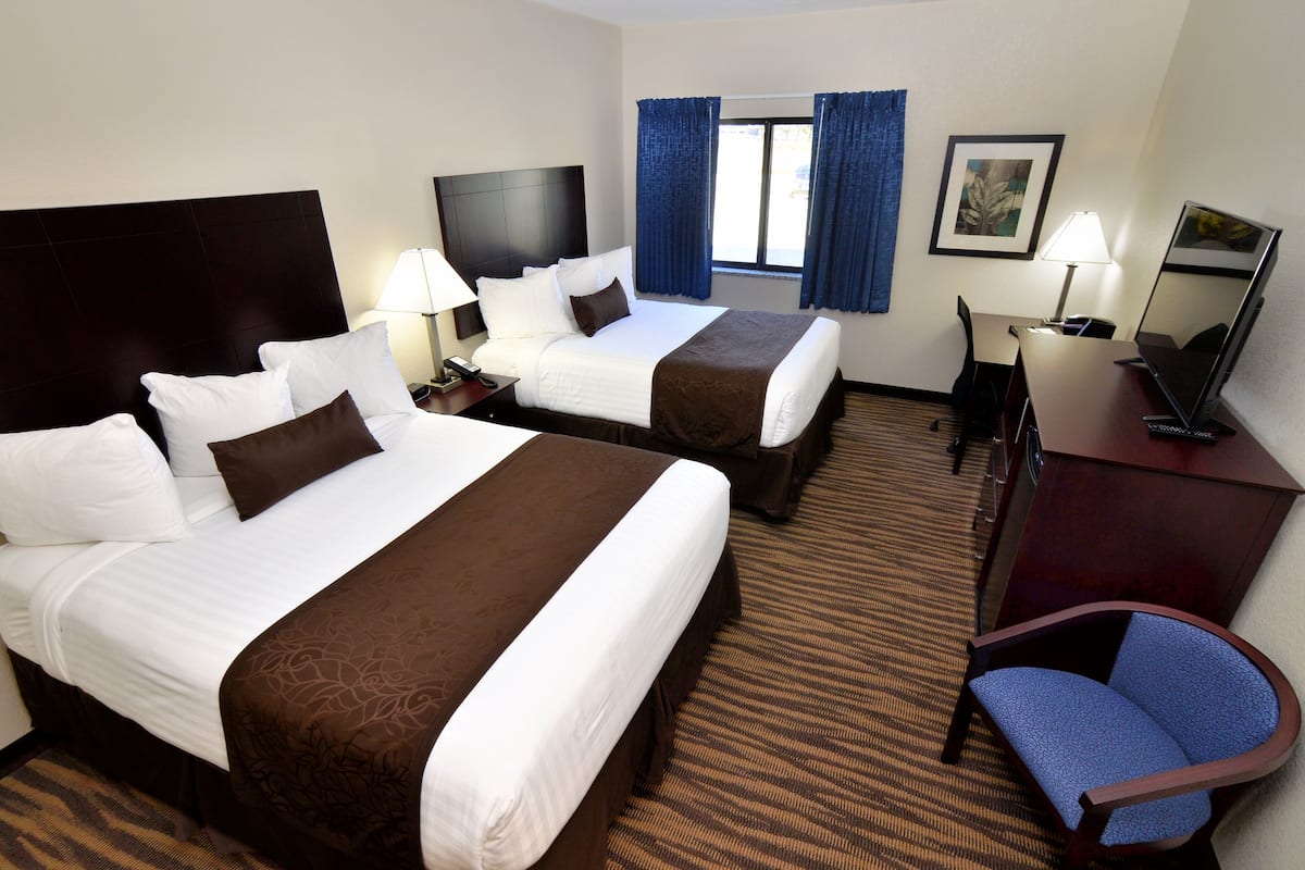 Ein Hotelzimmer mit zwei Betten, einem Schreibtisch, einem Stuhl, einem Fernseher und einem Fenster mit Vorhängen.