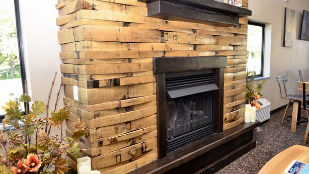 A rustic fireplace with a wooden mantel, a seating area with a chair, and a vase with flowers.