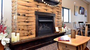 A fireplace with a wooden mantel, a table with a book, and a chair.