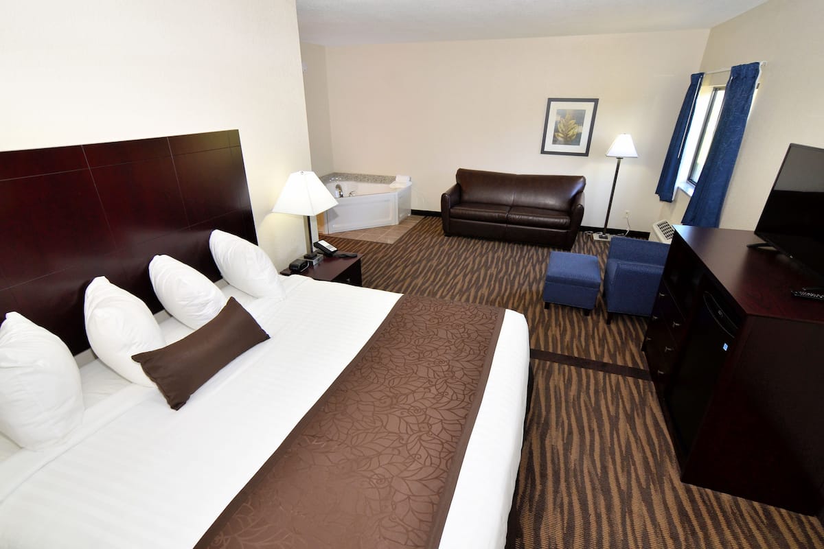 Ein Hotelzimmer mit einem großen Bett, einer Sitzecke, einem Schreibtisch mit Computer, einer Lampe, einem Fernseher und einer Badewanne.