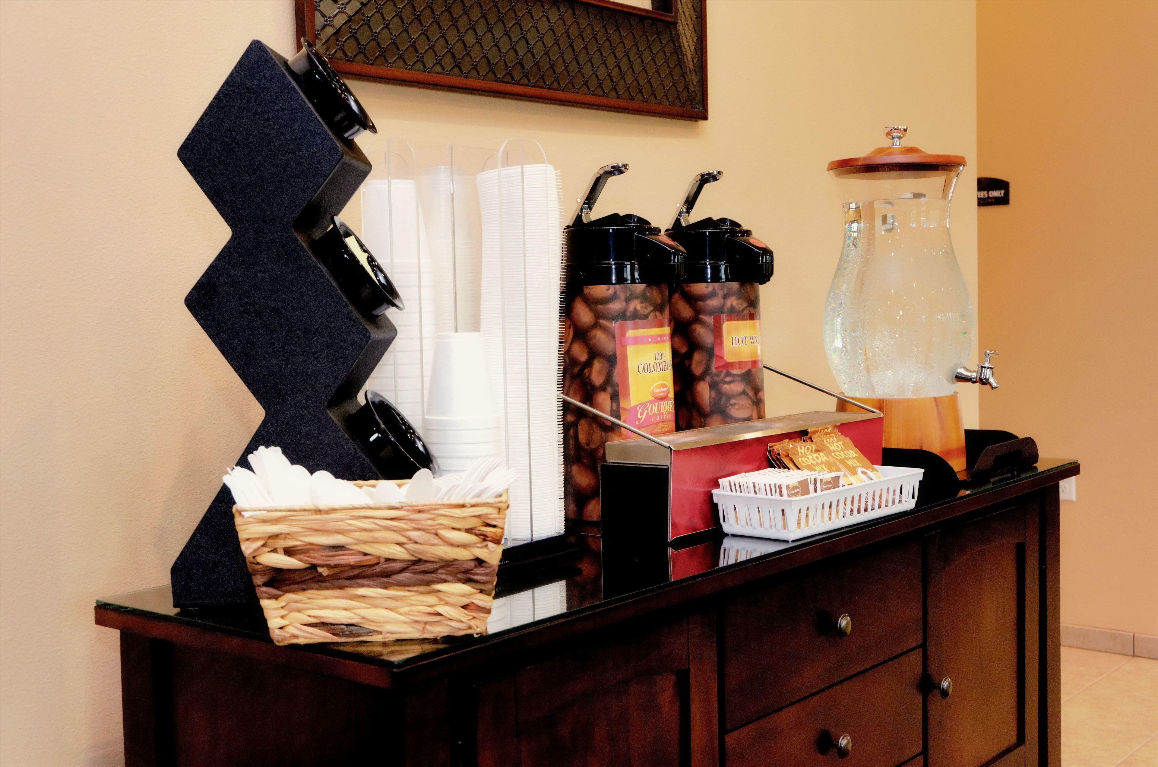A buffet setup with coffee dispensers, a pitcher of water, and a basket of bread.