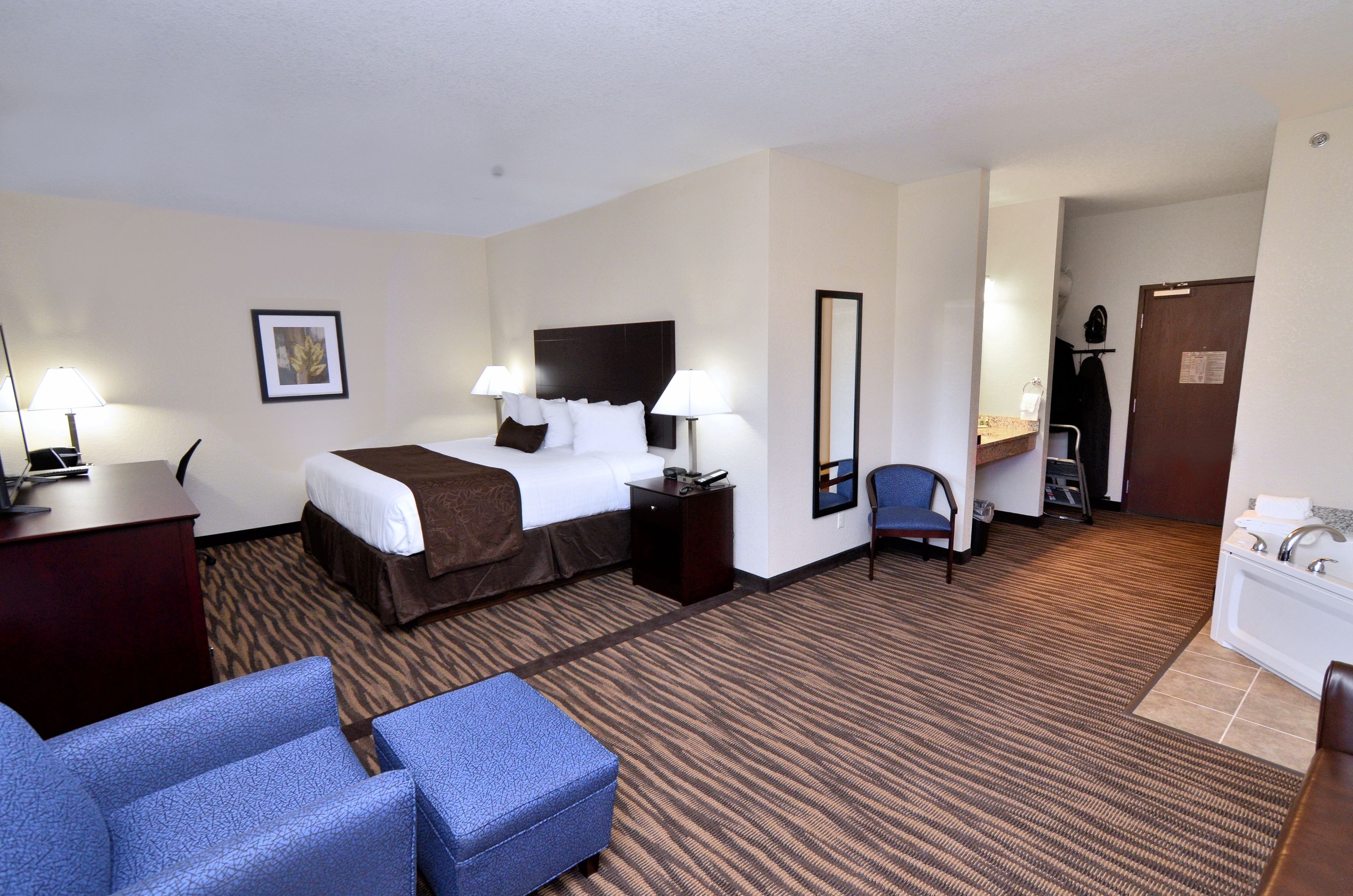 A hotel room with a bed, two bedside tables, a desk, a chair, a mirror, and a bathroom.