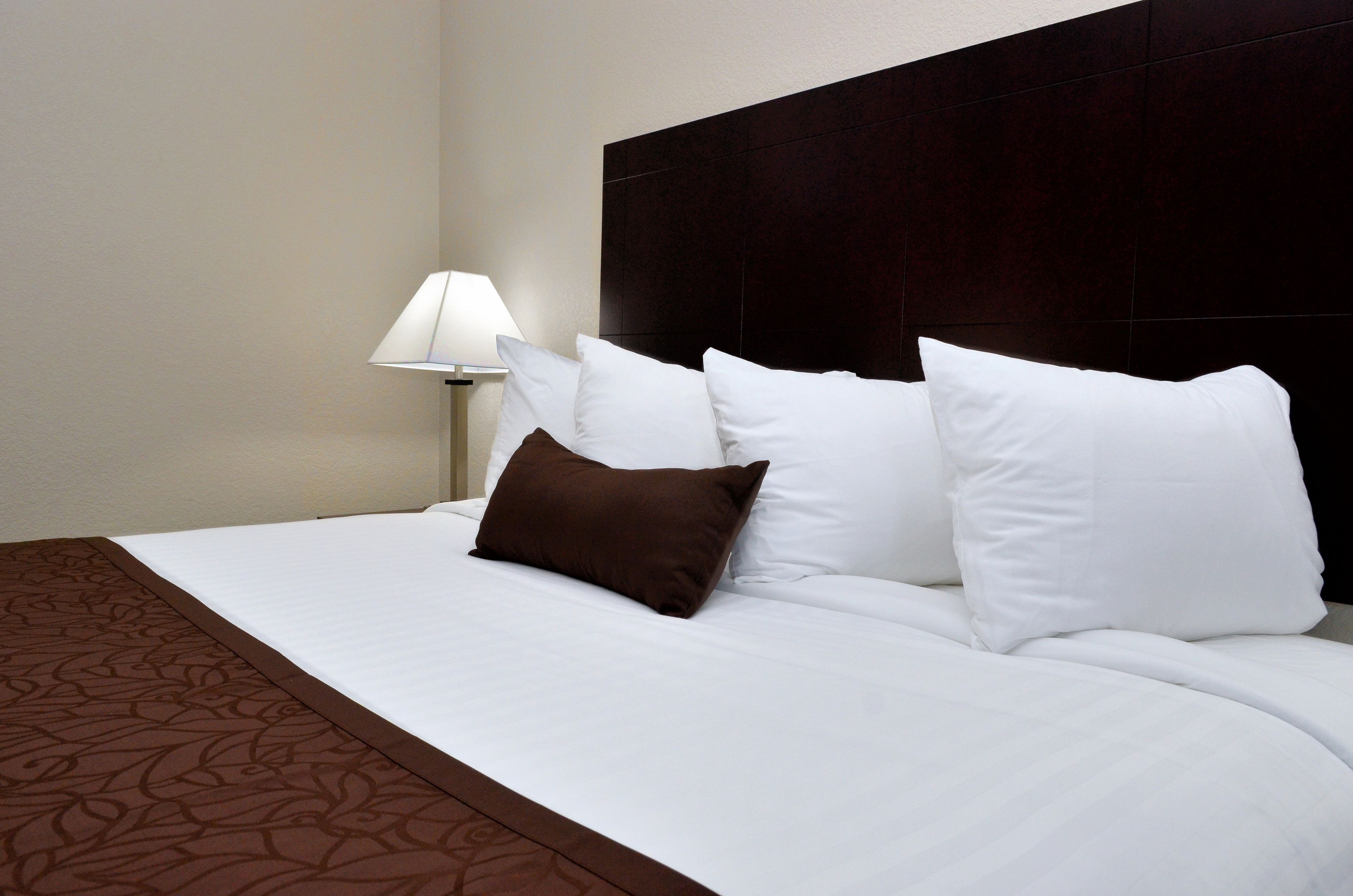 Een hotelkamer met een groot bed, witte beddengoed, een donker hoofdeinde en een bedlamp.